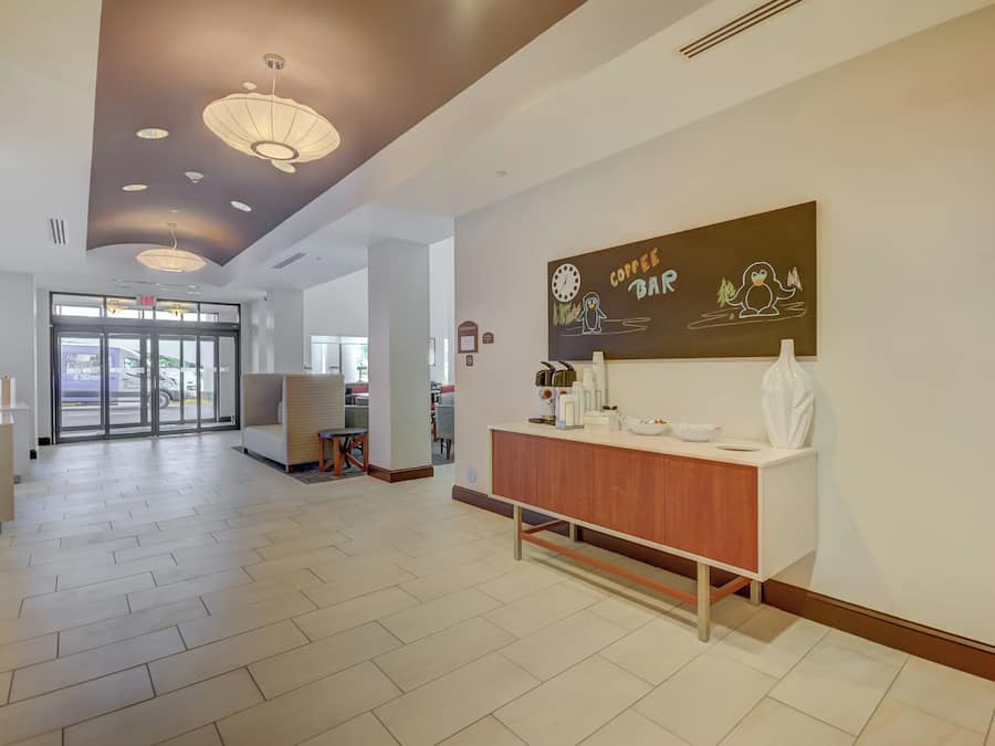 Un vestíbulo de hotel con una recepción, una cafetería y una zona de estar.