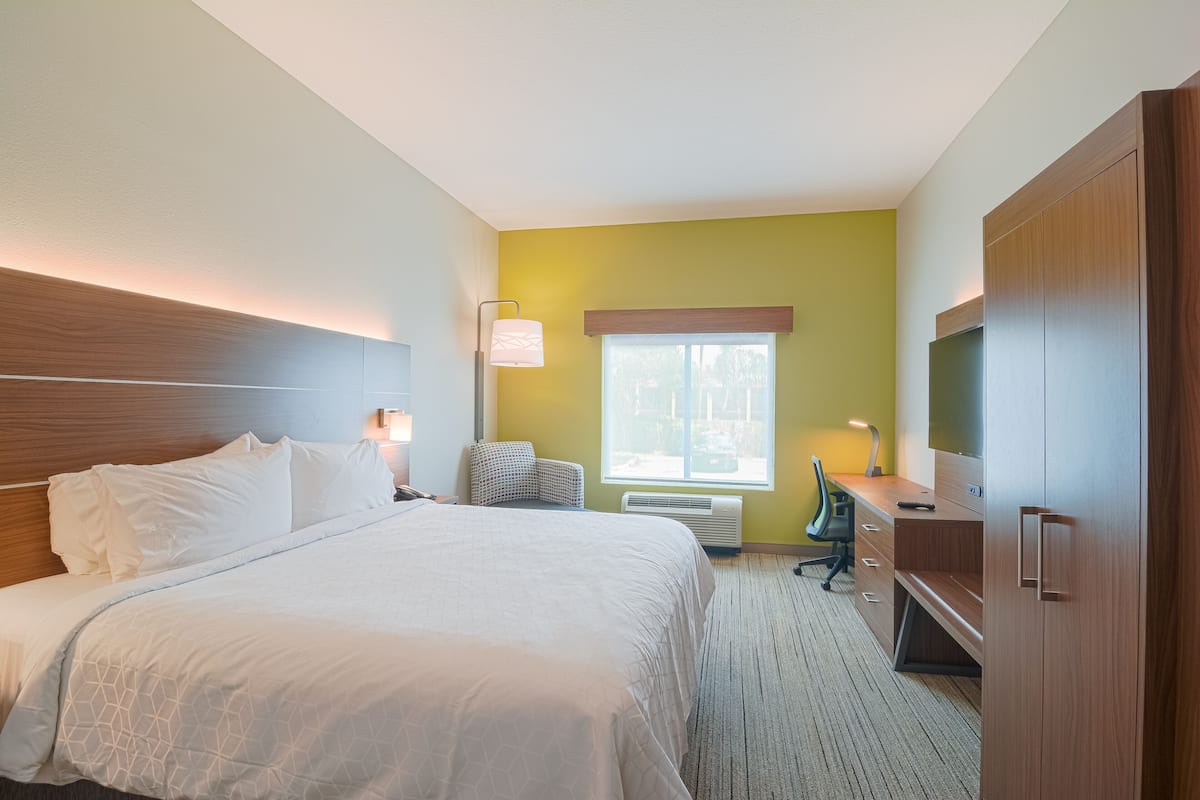 Ein Hotelzimmer mit einem großen Bett, einem Schreibtisch mit Stuhl, einem Fernseher und einem Fenster mit Aussicht.