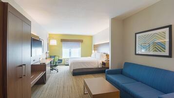 A hotel room with a bed, a blue sofa, a desk with a chair, a television, and a framed picture on the wall.