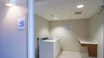 A laundry room with a washing machine, a sink, and signs indicating guest laundry is open 24 hours.