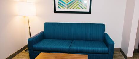 Una habitación con un sofá azul, una mesa de centro de madera, una lámpara y un cuadro abstracto enmarcado en la pared.