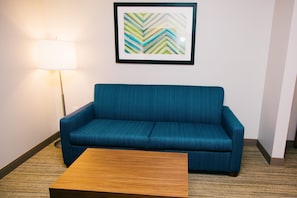 A room with a blue sofa, a wooden coffee table, a lamp, and a framed abstract art piece on the wall.