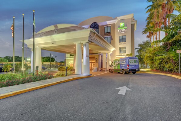 Entrada de un hotel con un toldo, una furgoneta y banderas.