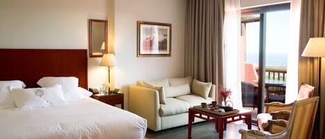 A hotel room with a bed, a sofa, a chair, a small table, and a balcony with a view.