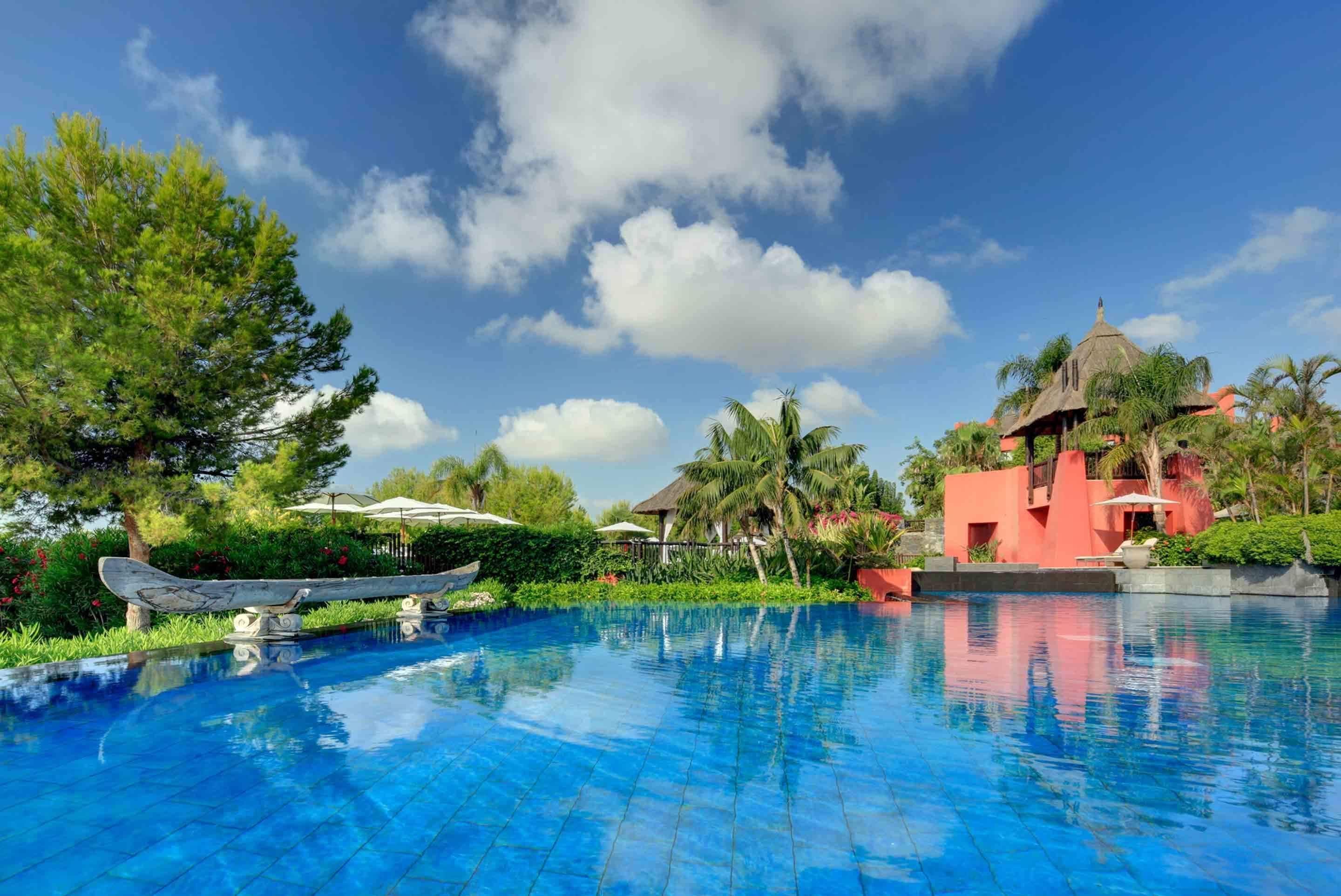 A swimming pool with a boat, surrounded by lush greenery and a clear blue sky.