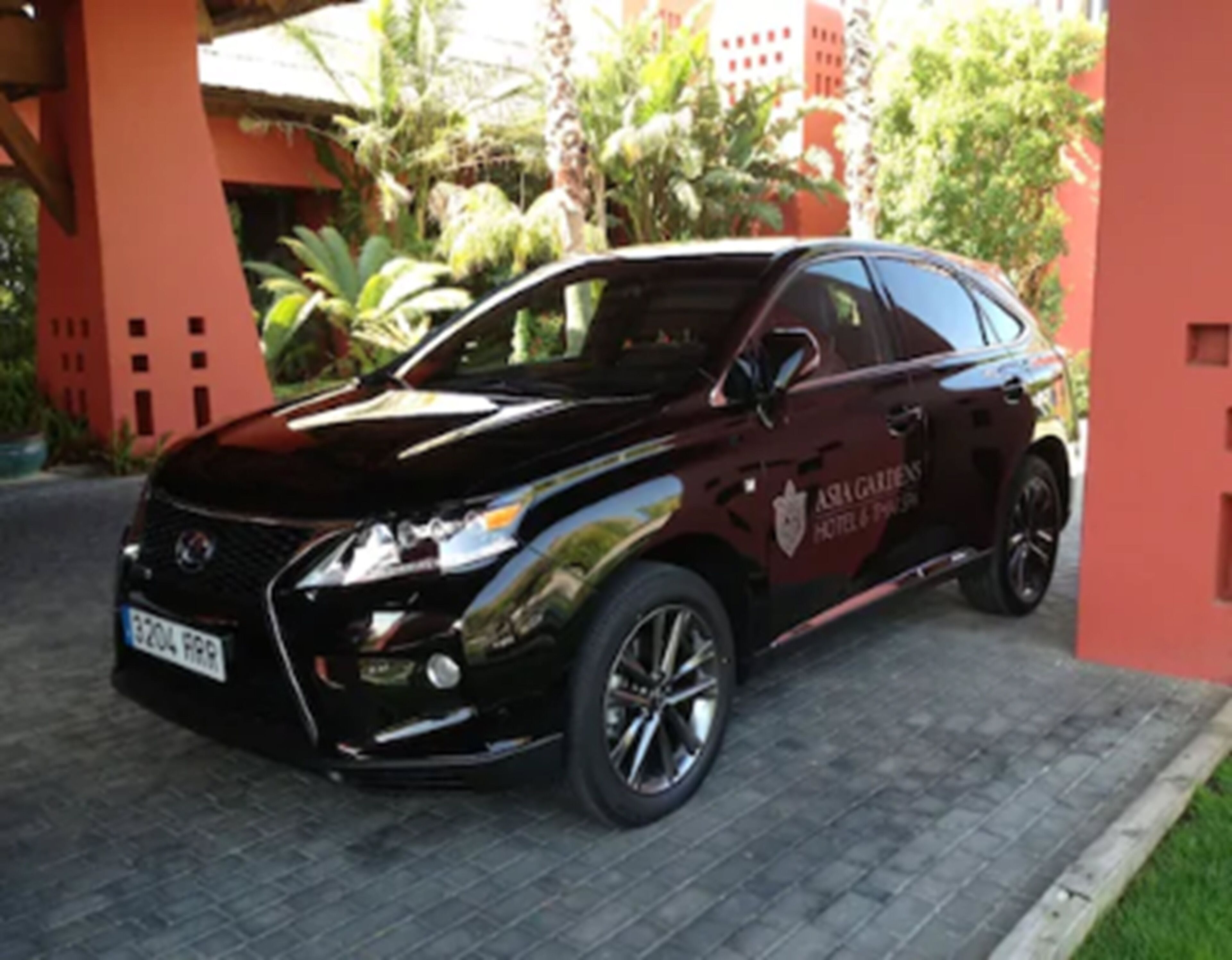 Un SUV negro estacionado frente a un edificio de fachada roja y un letrero que dice "Asian Gardens Hotel & Spa".