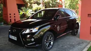 Un SUV negro estacionado frente a un edificio de fachada roja y un letrero que dice "Asian Gardens Hotel & Spa".