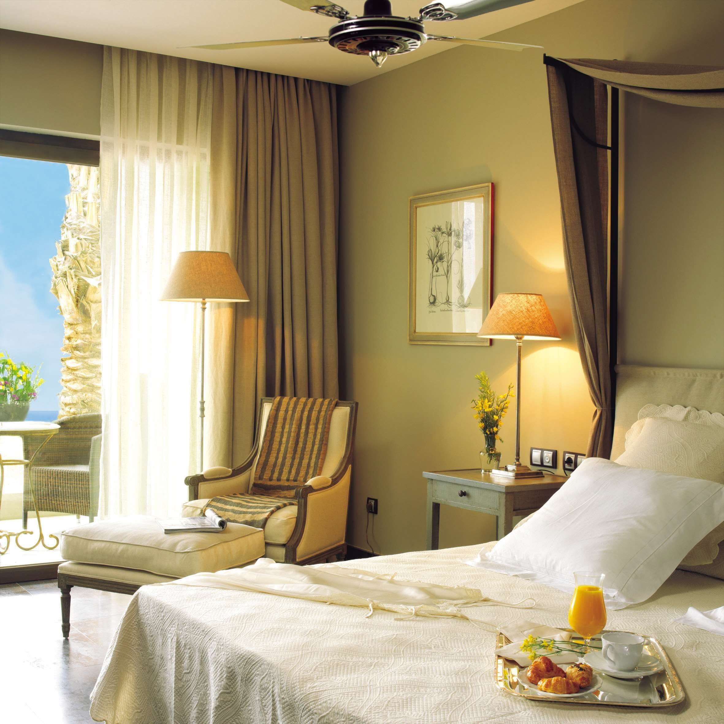 Habitación de hotel con cama, una silla, mesita de noche con lámpara y bandeja con alimentos para el desayuno.