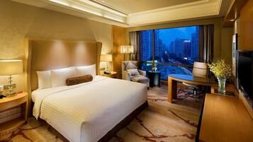 A hotel room with a large bed, a desk, a chair, a TV, and a view of a cityscape.
