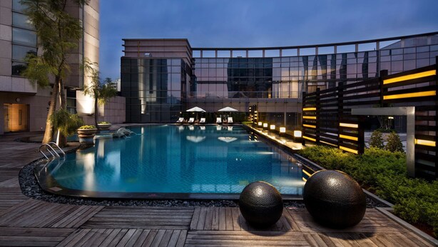 A swimming pool with lounge chairs and umbrellas, surrounded by modern buildings and well-maintained landscaping. - Hilton Xiamen (Xiamen)