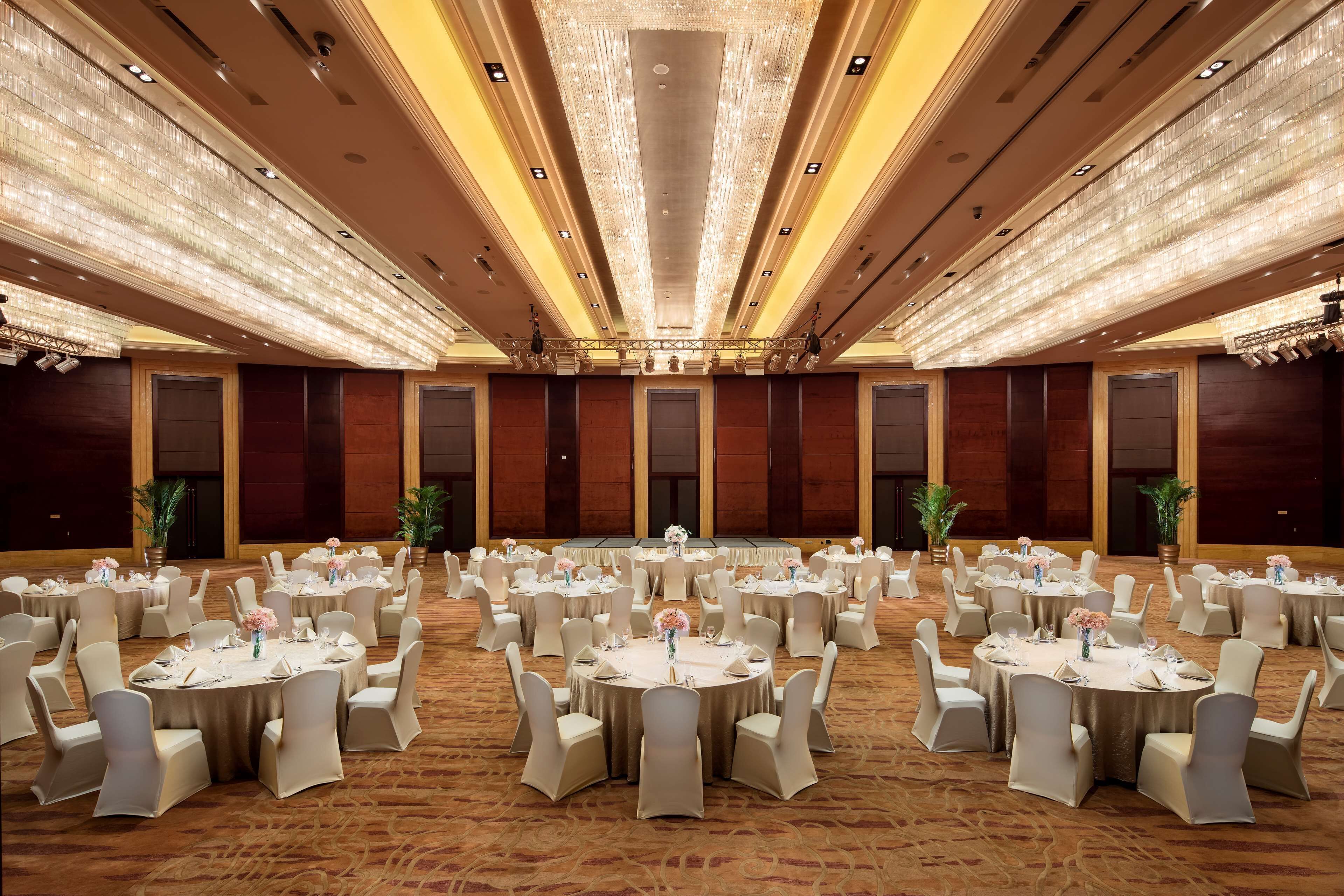A large banquet hall with round tables, each set with white tablecloths and chairs, and a chandelier overhead.