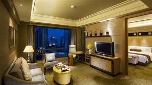 A hotel room with a sofa, armchair, TV, minibar, and a city view. - Hilton Xiamen (Xiamen)