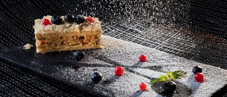 A slice of cake with berries on a black plate, dusted with powdered sugar, on a textured surface.