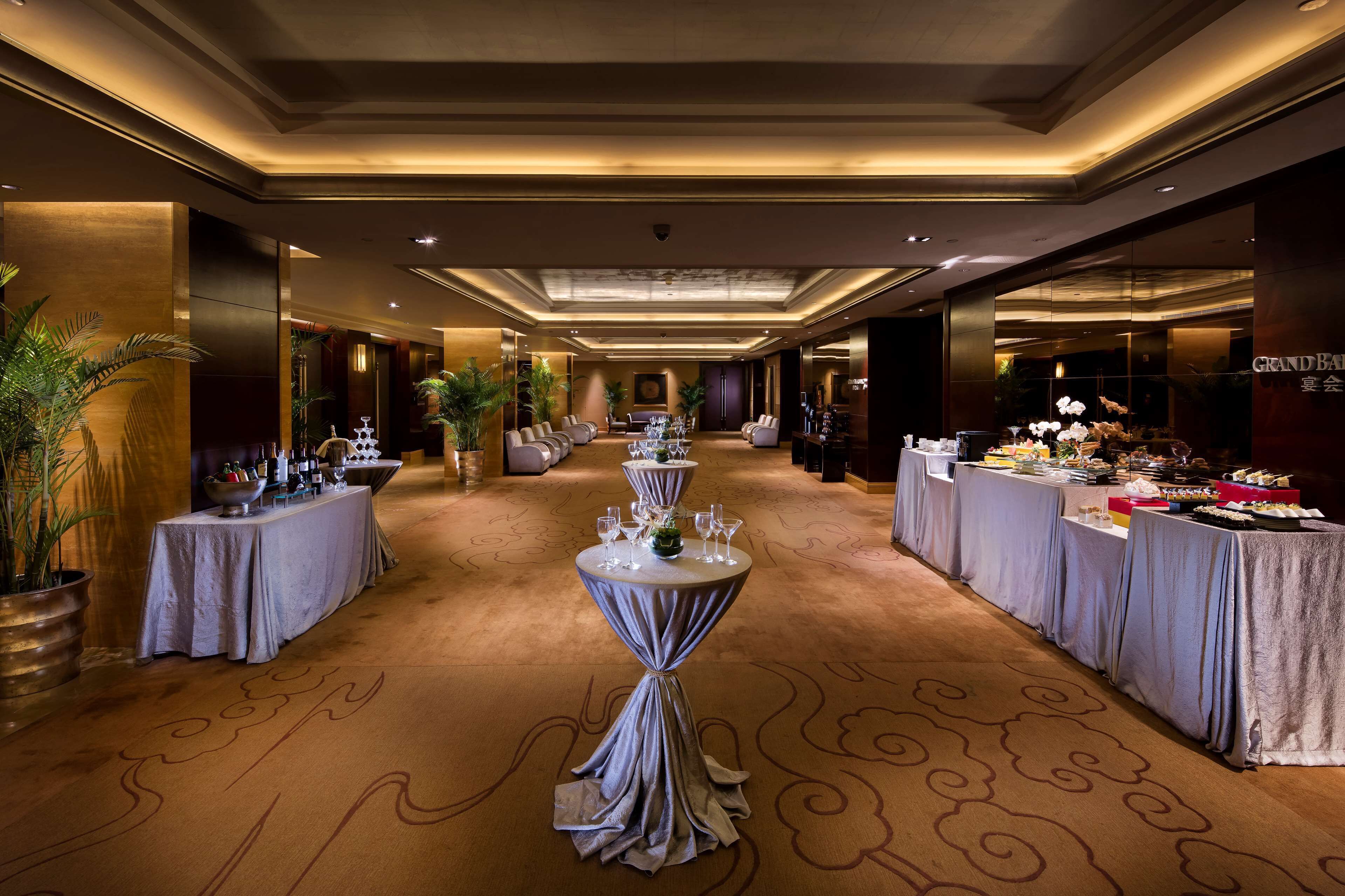 A hotel lobby with a long reception desk, multiple tables with chairs, and a buffet area.
