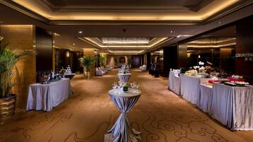 A hotel lobby with a long reception desk, multiple tables with chairs, and a buffet area.