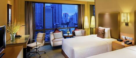Habitación de hotel con dos camas, un escritorio, una silla, un televisor y vista a la ciudad.