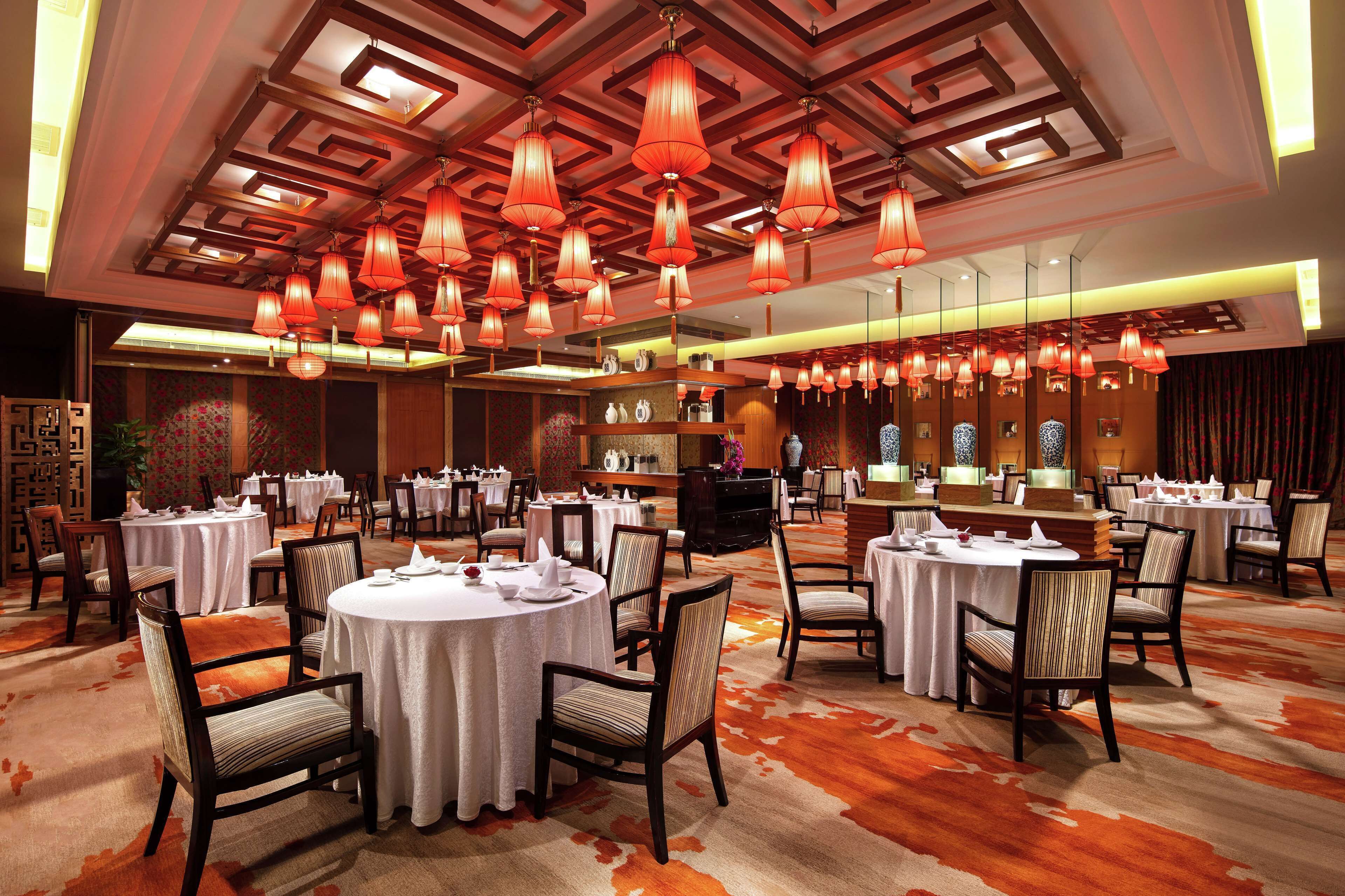A hotel dining area with round tables, chairs, and red hanging lamps.