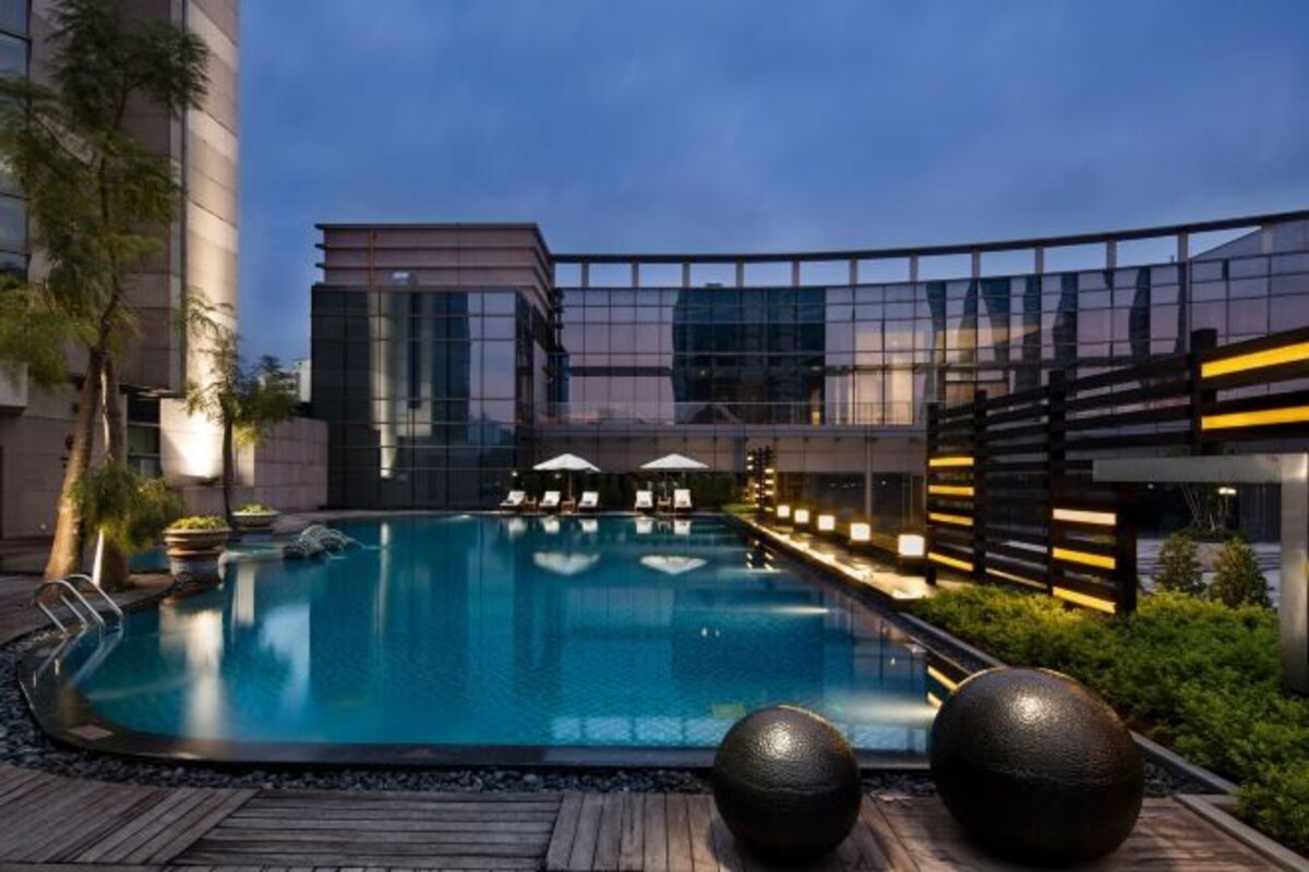 A swimming pool with lounge chairs and umbrellas, surrounded by modern buildings and greenery.