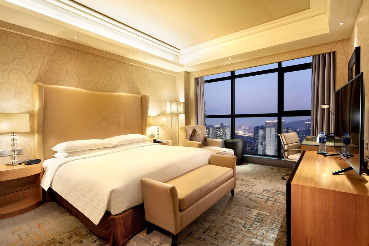 A hotel room with a large bed, a desk, and a view of the cityscape.