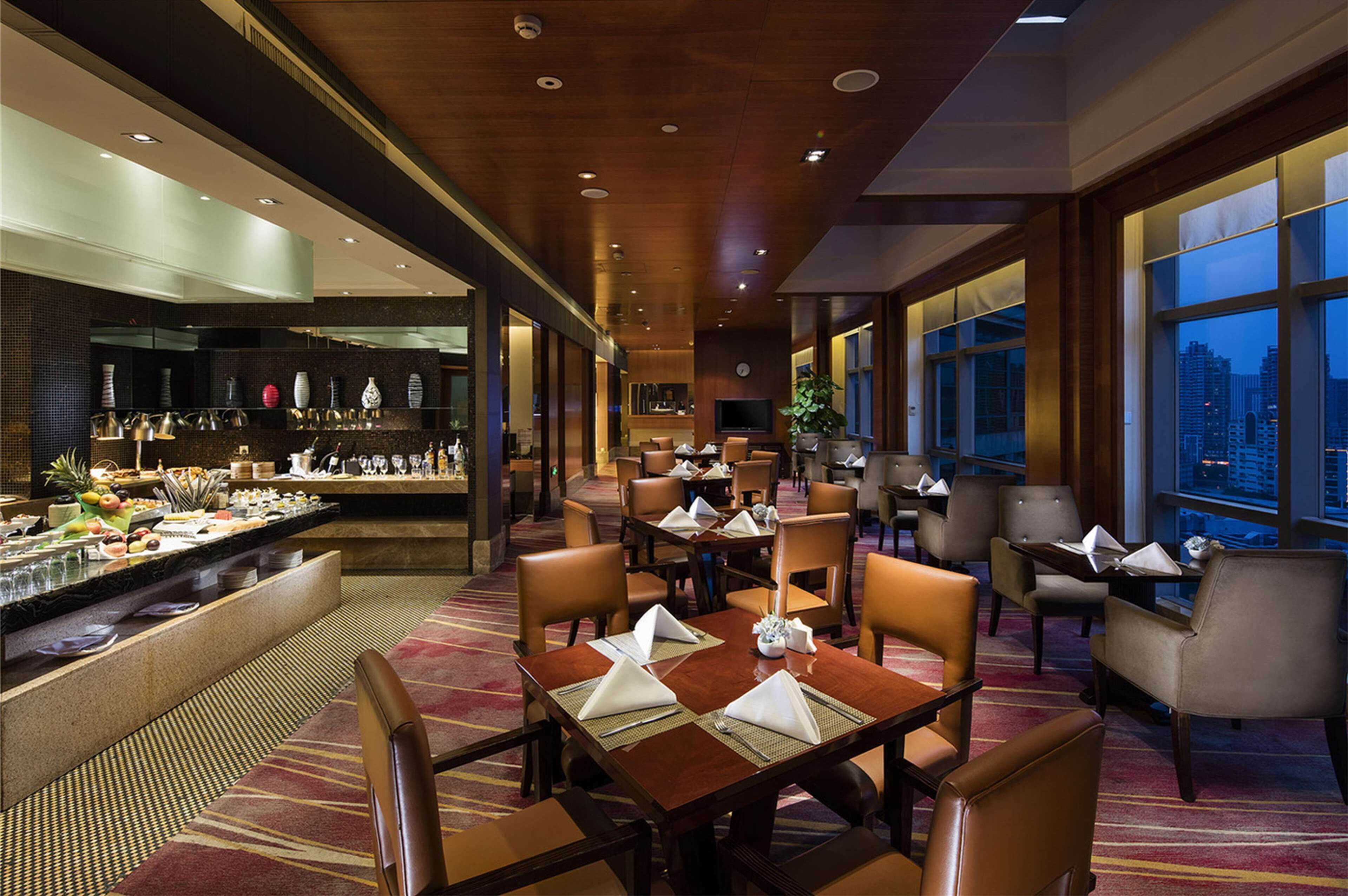 A hotel lobby with a dining area, a bar, and large windows offering a city view.