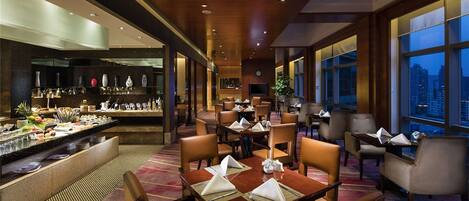 A hotel lobby with a dining area, a bar, and large windows offering a city view.