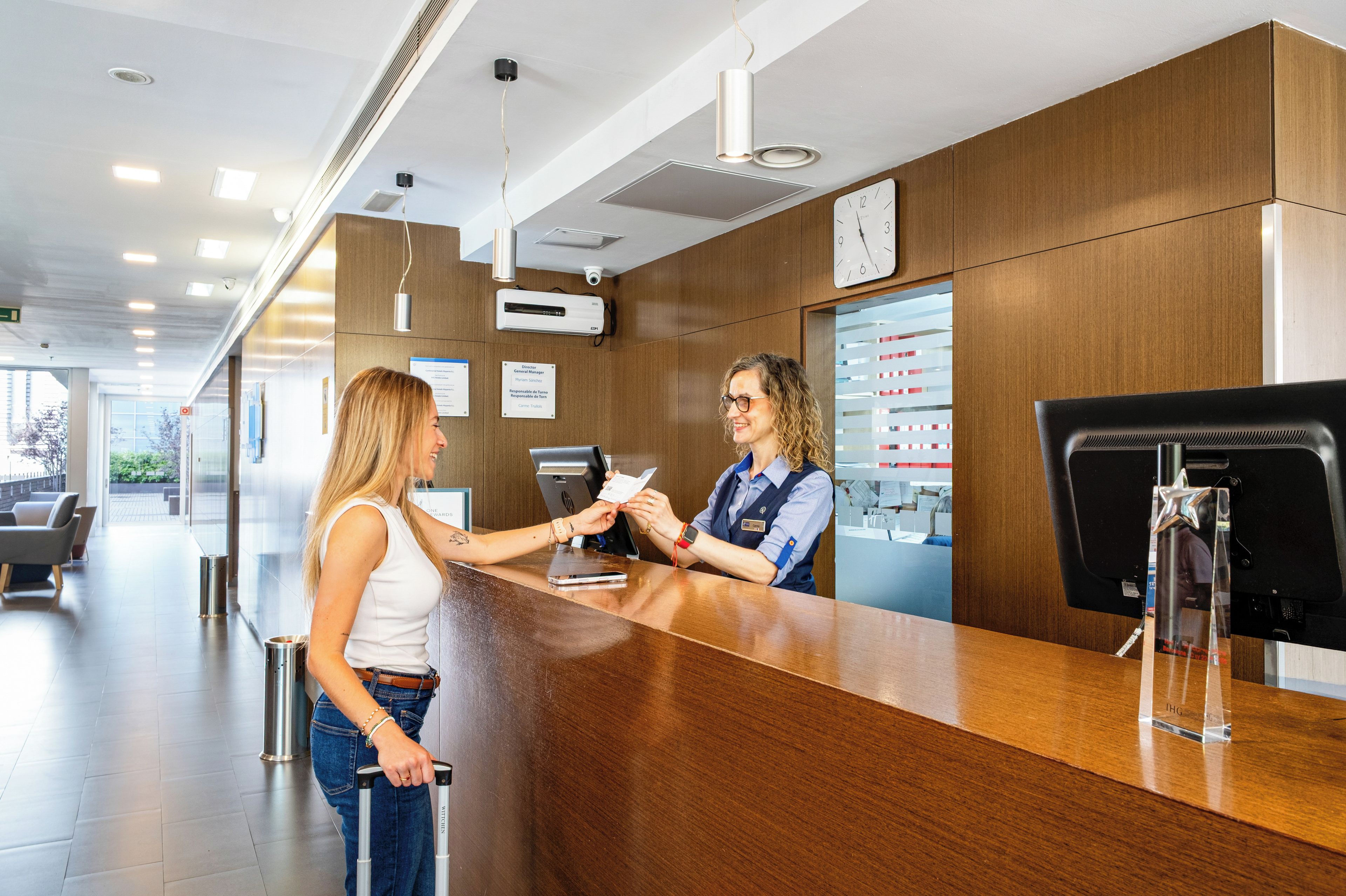 A reception area with a wooden reception desk, a clock, and a digital display.