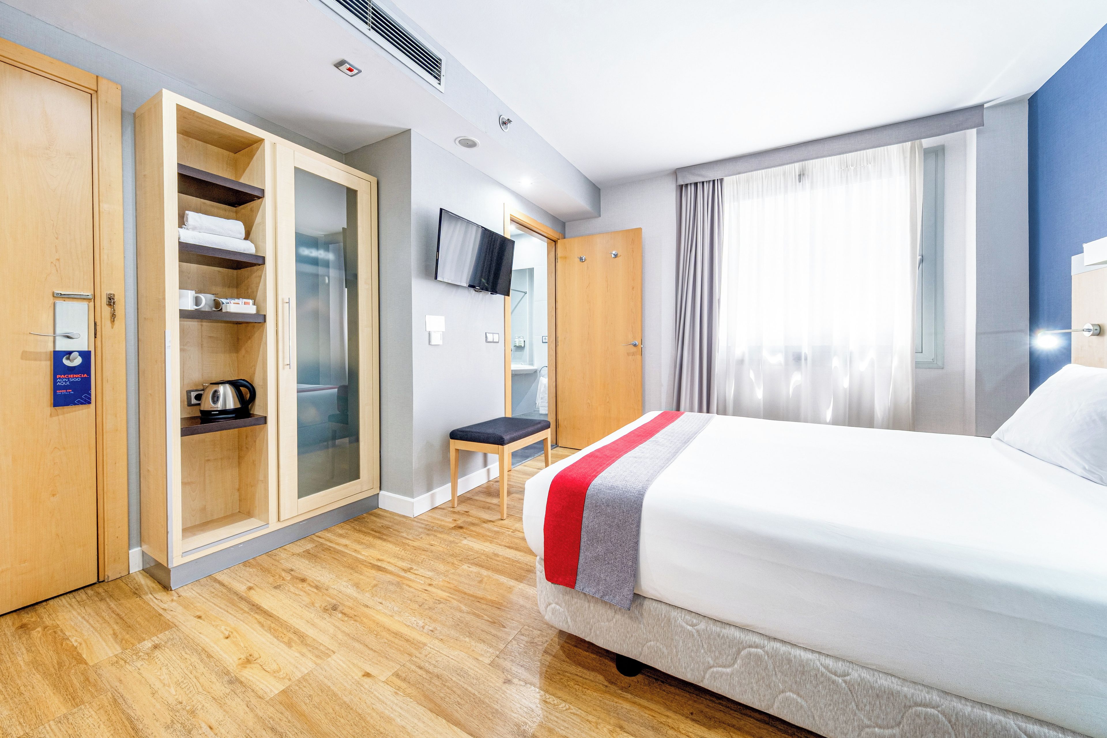 Une chambre d’hôtel avec un lit, une télévision, une armoire et une salle de bain visible à travers une porte ouverte.