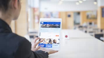 Una persona sosteniendo una tablet que muestra un sitio web de reservas de hotel con opciones para buscar y reservar.