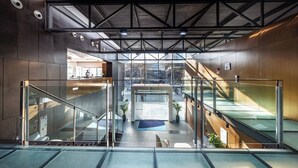 Un interior modern amb baranes de vidre, una escala central i vistes a través de grans finestres.