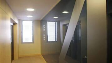 A hallway with a carpeted floor, recessed ceiling lights, and a trash can.