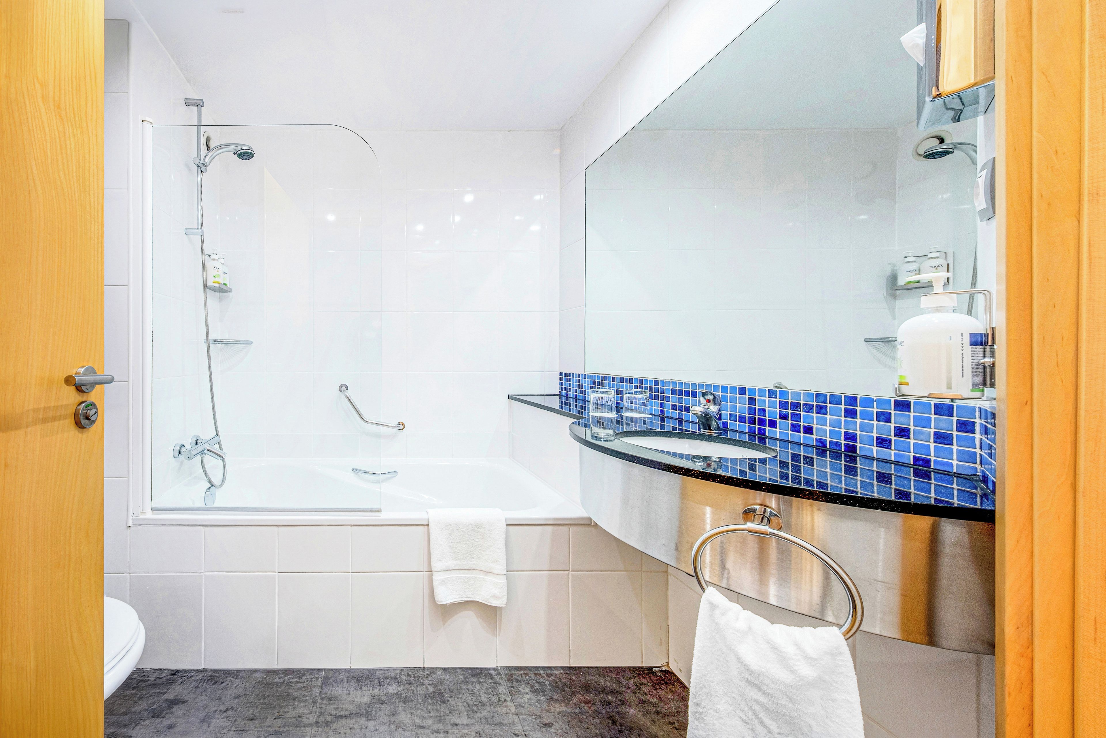 Un baño moderno con ducha envuelta en vidrio, una bañera blanca, un tocador con azulejos azules y un espejo grande.