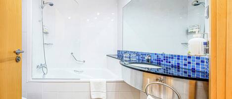 Un baño moderno con ducha envuelta en vidrio, una bañera blanca, un tocador con azulejos azules y un espejo grande.