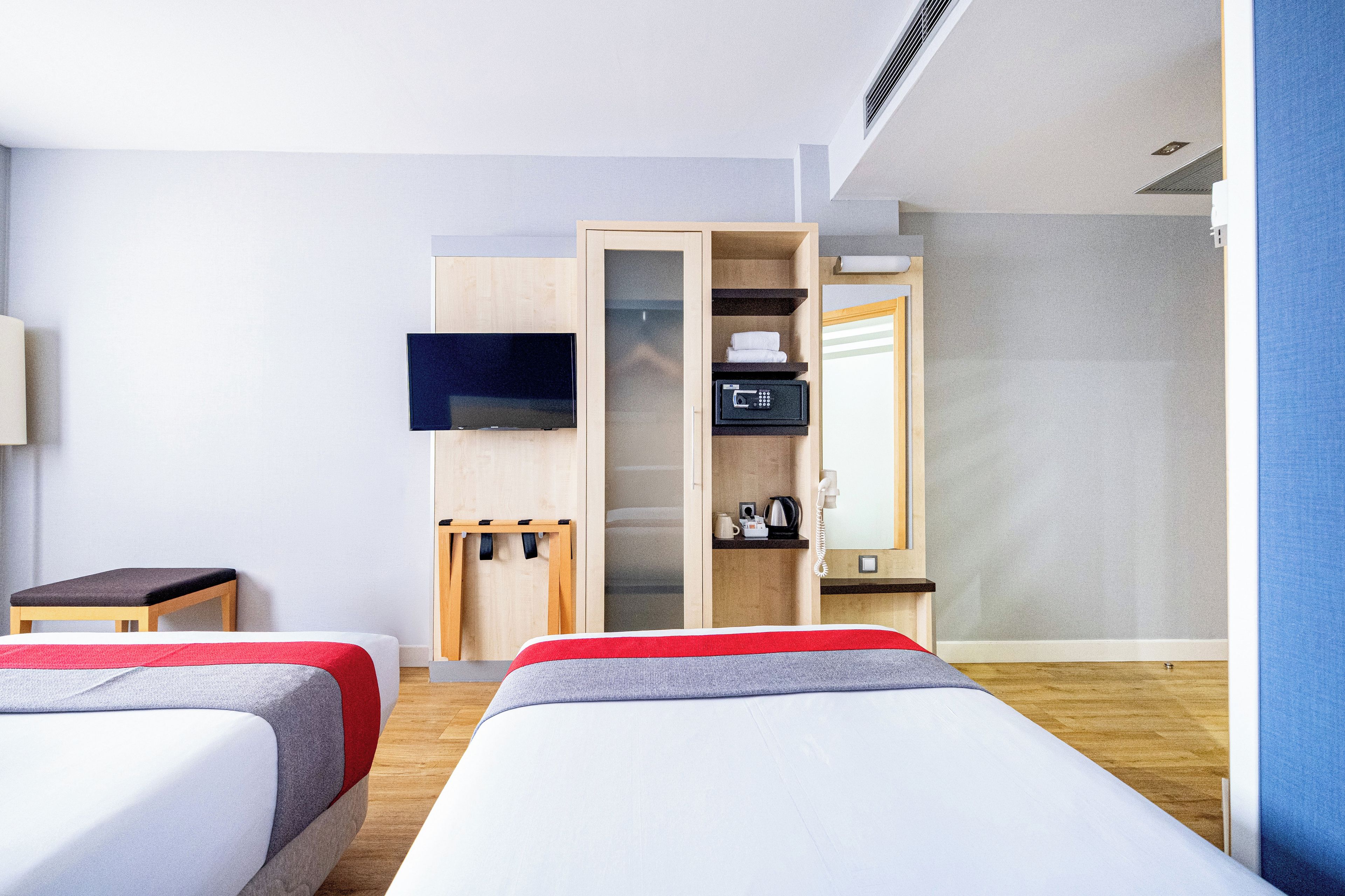 A hotel room with two beds, a TV, a minibar, and a mirror.