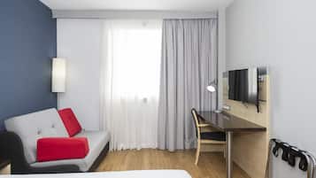 Habitación de hotel con cama, escritorio, silla, televisor y ventana con cortinas.