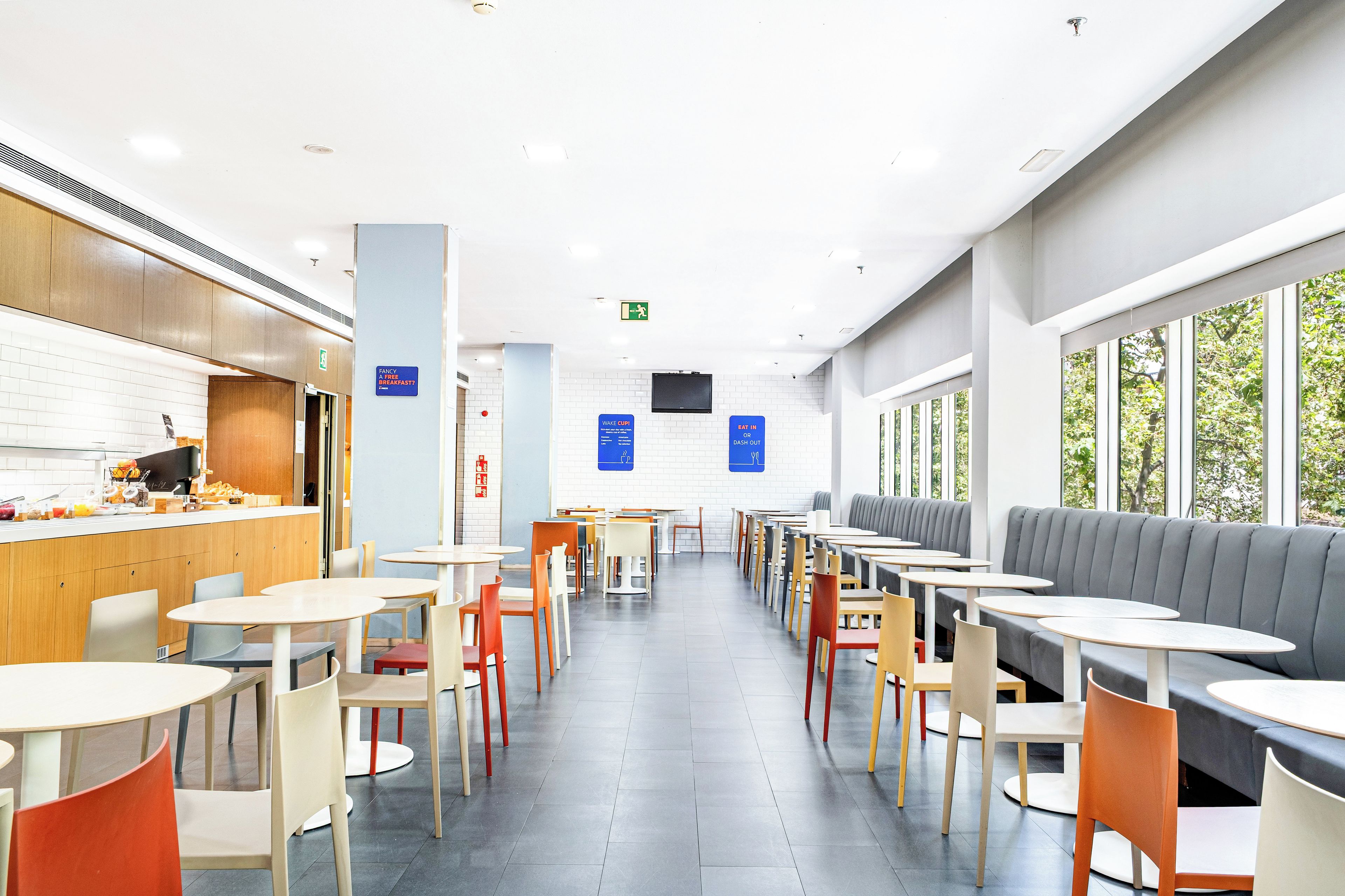 Un café moderno con diversas opciones de asientos, incluidas mesas y cabinas, y un área de desayuno a la vista.