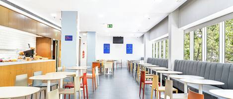 Un café moderno con diversas opciones de asientos, incluidas mesas y cabinas, y un área de desayuno a la vista.