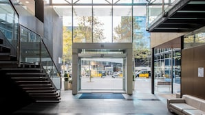 Entrada d'un edifici modern amb una porta de vidre, una escala a l'esquerra i una banca a la dreta.