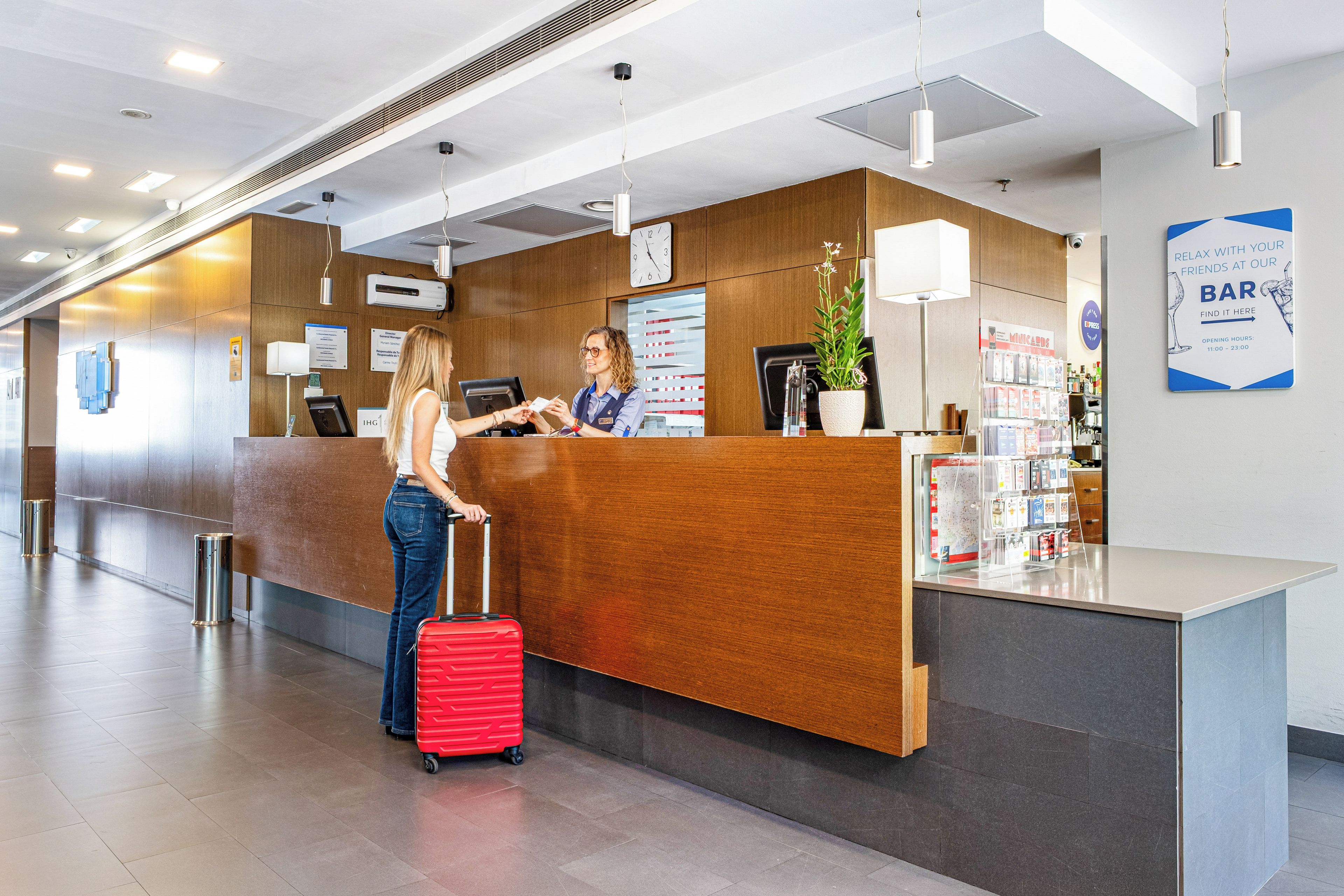 A reception desk with a digital clock, a bar sign, and a plant.