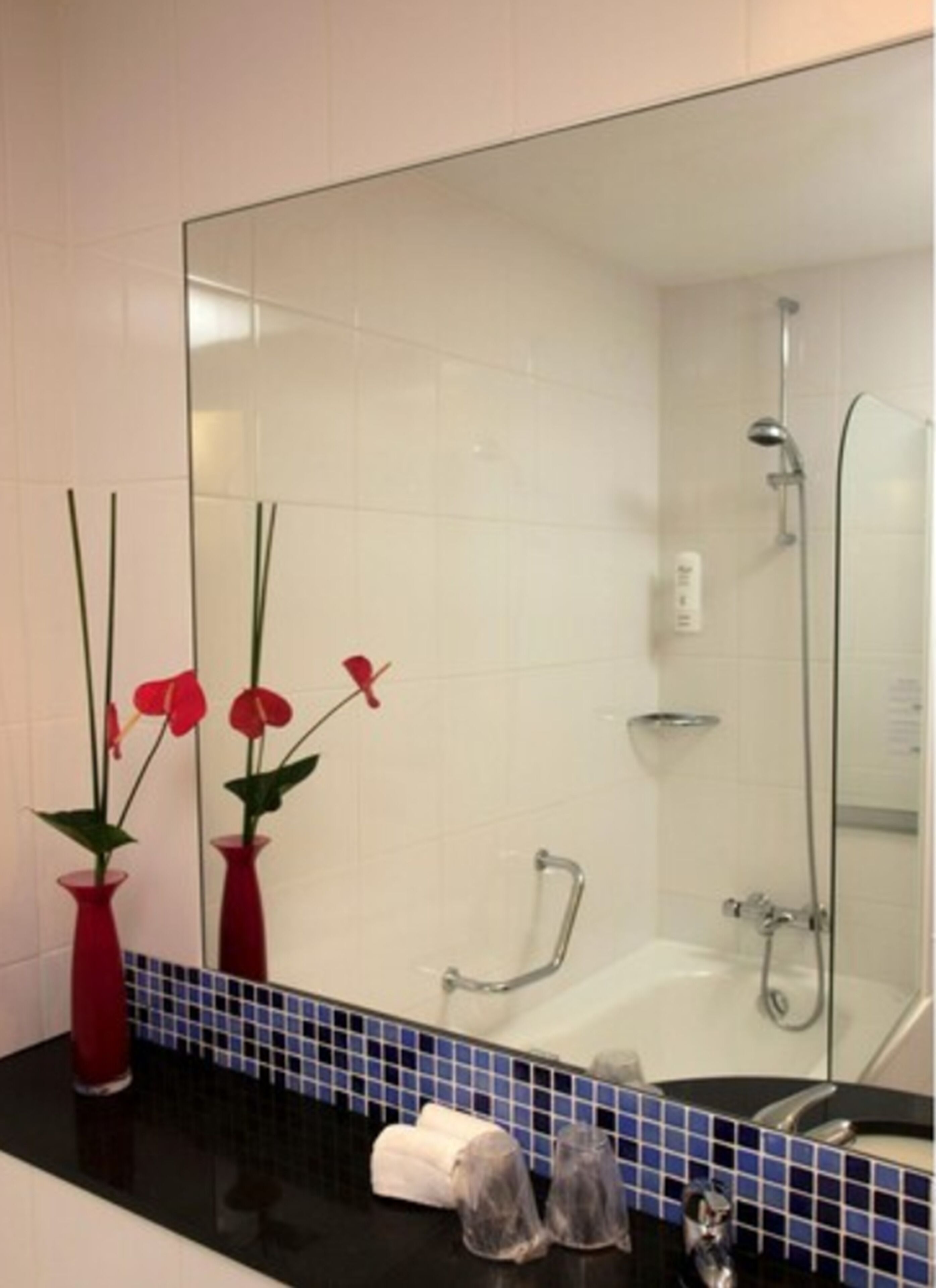 A bathroom with a bathtub, a shower, and a mirror. There are two red vases with flowers on the counter.