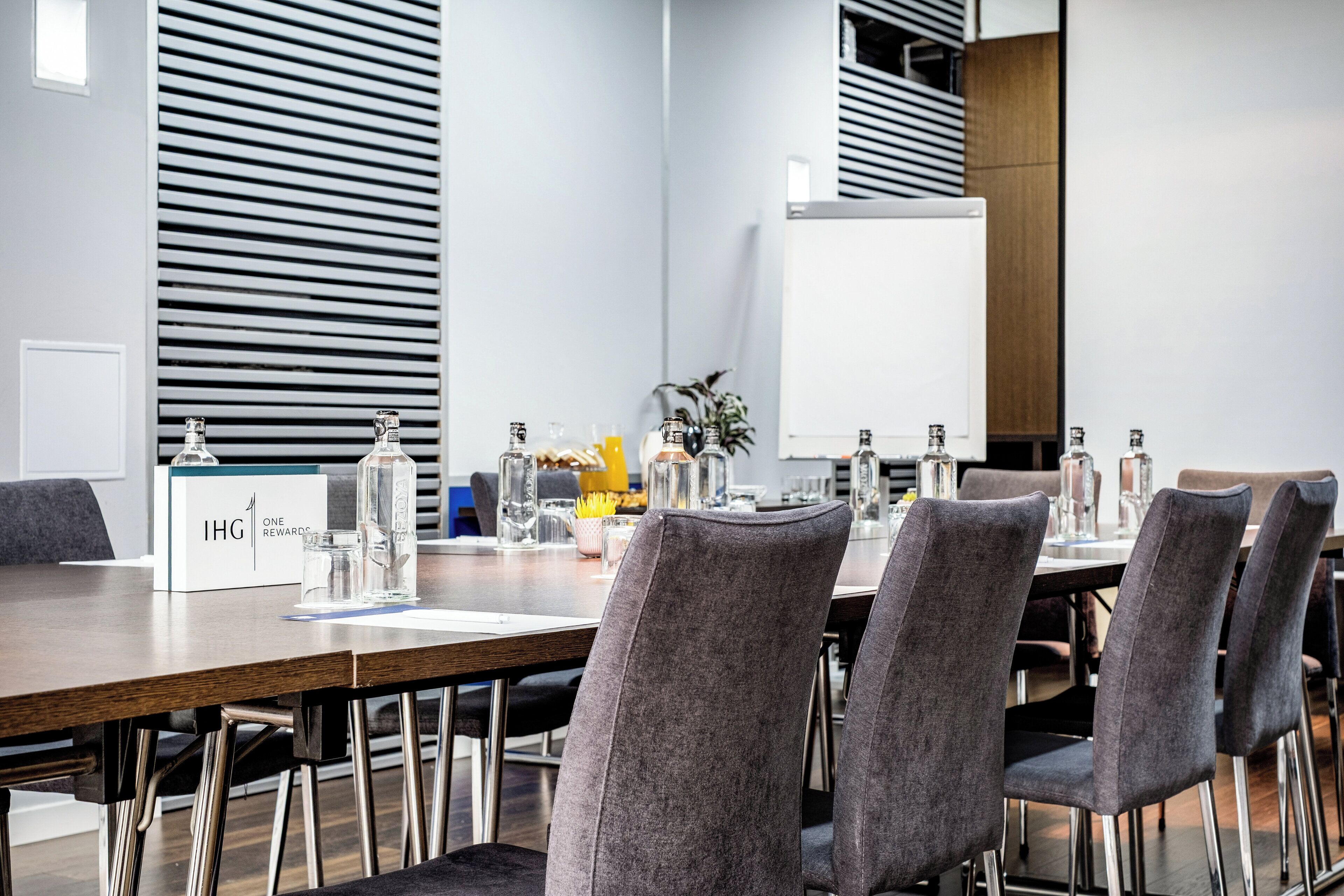 A conference room with a long table, grey upholstered chairs, and a whiteboard.