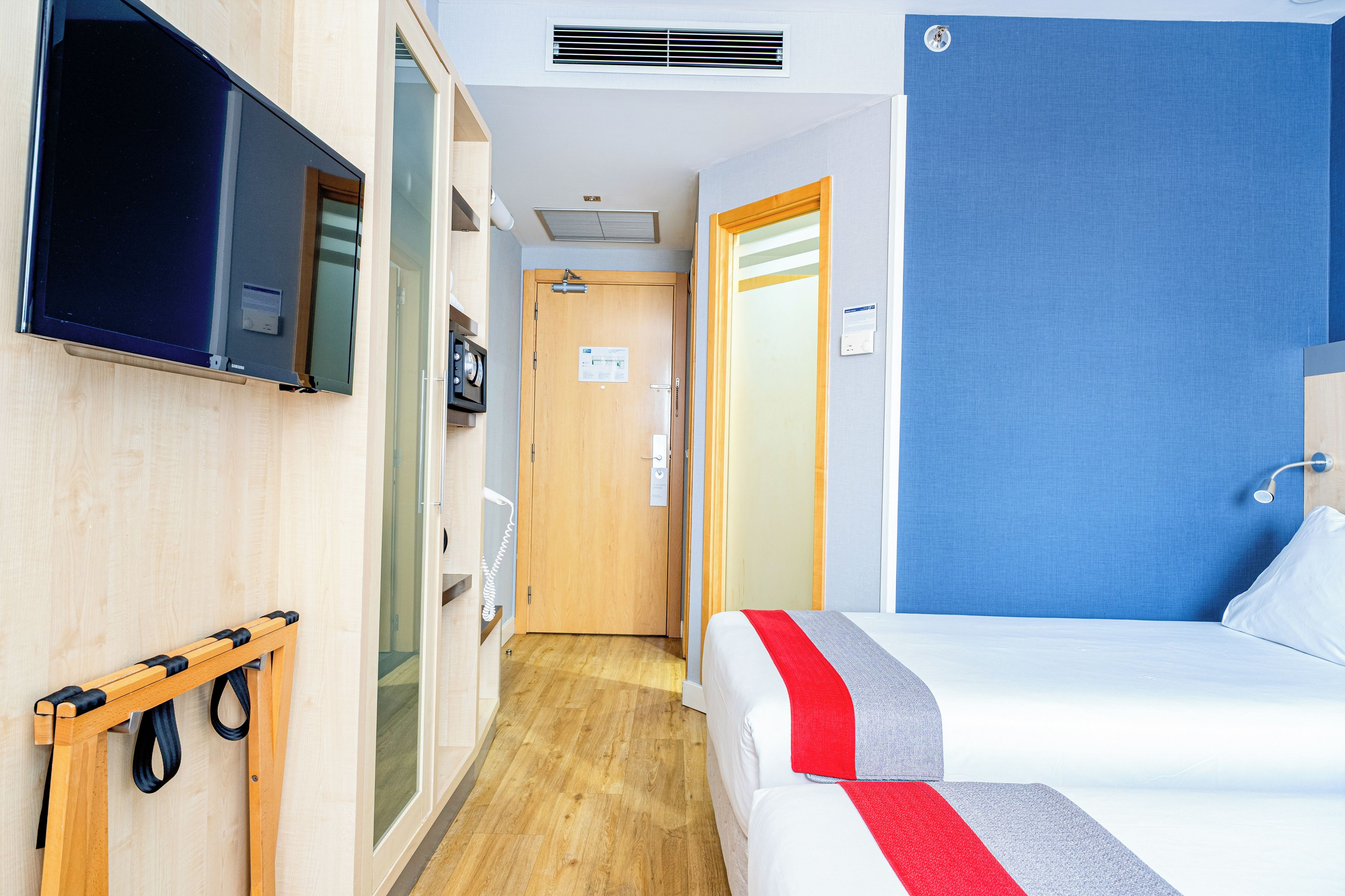A hotel room with a bed, a television, a shower, and a wooden bench.