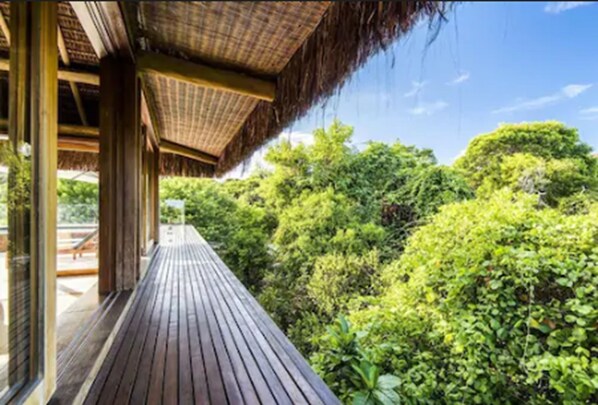 Une terrasse en bois mène à une construction à toit de chaume, d’où l’on peut admirer une végétation luxuriante.