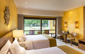 Ein Hotelzimmer mit zwei Betten, einem Essbereich mit Tisch und Stühlen, einer Hängematte im Freien und Blick ins Grüne.
