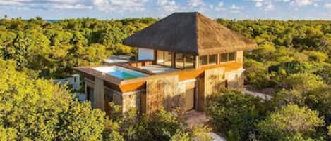 A thatched-roof bungalow with a pool, surrounded by dense greenery.