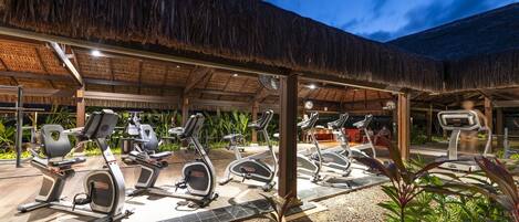 An outdoor gym area with exercise equipment under a thatched roof structure.