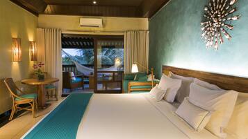 A hotel room with a large bed, a small table with chairs, a hammock, and a view of palm trees.