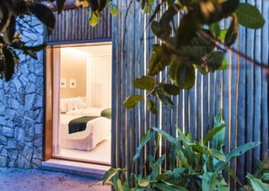 Una habitación de hotel moderna con fachada de piedra, un gran ventanal y una cama con cabecera verde.