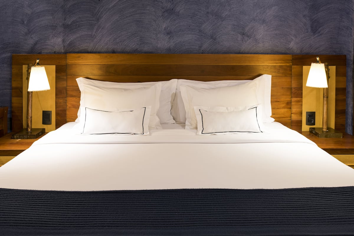 A neatly made bed with white linens and a dark blue accent at the foot.