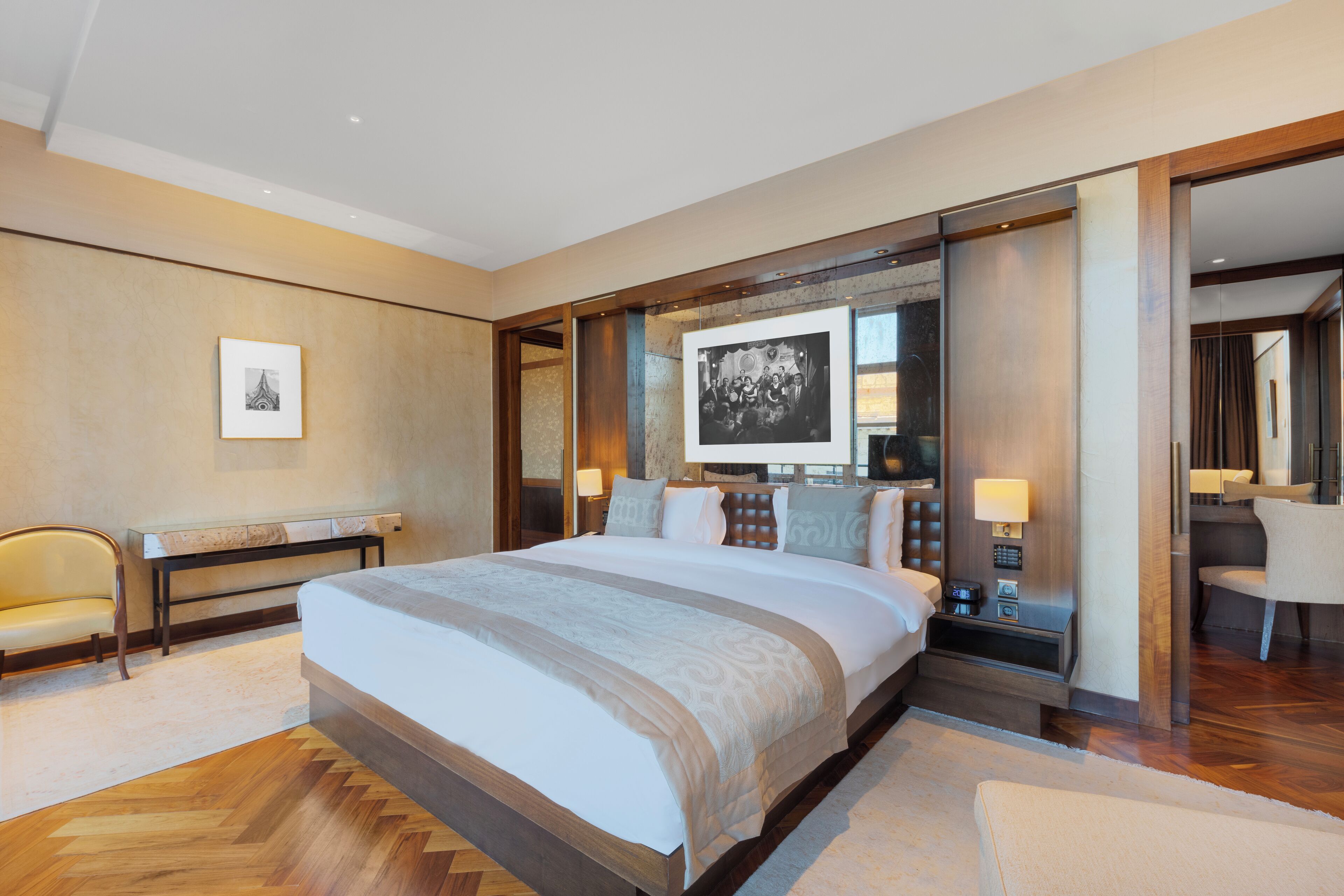 A modern hotel room with a large bed, a desk, and a chair. There are two framed pictures on the wall.
