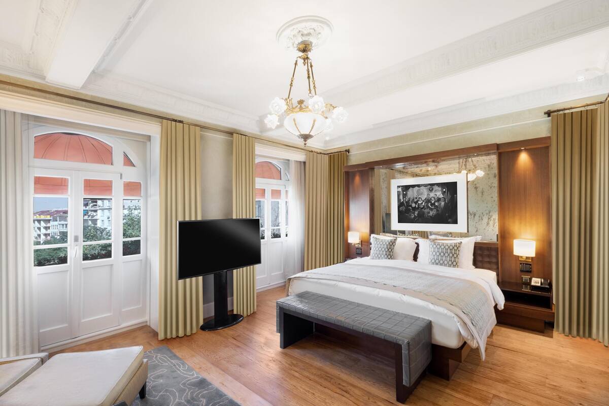 Una habitación de hotel amplia con una cama grande, televisión y un banco.
